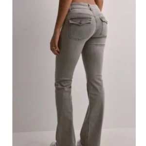 Grå bootcut jeans med fickdetaljer - Snygga grå jeans med bootcut passform och coola fickdetaljer bak. Jeansen har låg midja och är tillverkade i ett mjukt denimtyg som sitter skönt. Perfekta för dig som vill ha en trendig och avslappnad look.