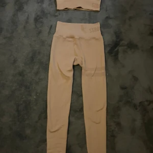 Beige leggings och träningsstopp från Stronger - Snygga beige leggings från Stronger med hög midja och ribbad struktur. Tillverkade i ett stretchigt material som består av 94% polyamid och 6% elastan. Perfekta för träning eller chill dagar, sitter tajt och följer kroppen.  