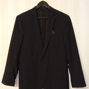 Svart kavaj med Filippa K märke i ull - Stilren svart kavaj från Filippa K i 100% ull. Klassisk modell med smal krage, en knapp framtill och innerficka. Perfekt för dig som gillar minimalistisk och tidlös design.                      Kan skickas med extra pris via post.