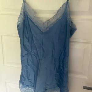 Spetslinne från intimissimi - Snygg blå linnetopp med tunna axelband och v-ringning. Toppen har fina spetsdetaljer längs halsringningen och nederkanten som ger en romantisk känsla. Perfekt att styla med jeans eller kjol för en trendig look.