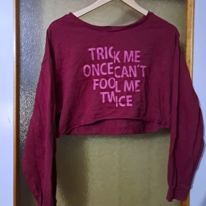 Vinröd croppad långärmad tröja - Cool vinröd croppad tröja med lång ärm och tryck i rosa text på framsidan: 'Trick me once can't fool me twice'. Perfekt för dig som gillar statement-plagg och avslappnad stil. Mjuk och skön i bomullsmaterial. Fint skick- ej använd så ofta :)