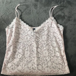 Ljusrosa spetslinne från Divided - Supersött ljusrosa linne från Divided med tunna axelband och v-ringning. Hela toppen är täckt av blommig spets och har en feminin, romantisk vibe. Perfekt att styla med jeans eller kjol för en trendig look.