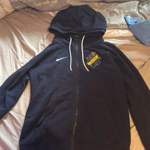 Mörkblå AIK hoodie från Nike - Säljer en mörkblå hoodie från Nike med AIK-logga på bröstet. Tröjan har huva med vita snören, dragkedja framtill och två stora fickor. Perfekt för dig som vill visa ditt AIK-stöd och gillar sportig stil. Nypris ca 1000
