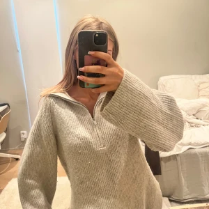 Beige ribbstickad half zip tröja - Supermysig beige ribbstickad tröja med half zip och breda ärmar. Tröjan har en avslappnad passform och slits i sidorna, perfekt för lager på lager. Passar dig som gillar en chill och oversized stil.
