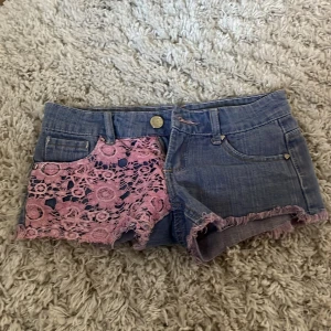 Jeansshorts med rosa spetsdetaljer - Snygga blå jeansshorts med råa kanter och unika rosa spetsdetaljer. Jag har köpt dom på plick men dom passade inte .