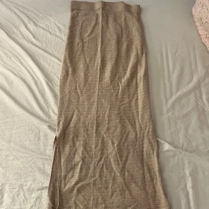 Beige stickad långkjol från KappAhl - Säljer en beige stickad långkjol från KappAhl i storlek S. Kjolen har en rak passform med diskreta horisontella ränder och en slits på sidan för extra rörelsefrihet. Perfekt för dig som gillar en enkel och stilren look.