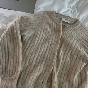 Beige ribbad kofta från Selected Femme - Supermysig beige kofta från Selected Femme med ribbat mönster och rund hals. Knäpps med knappar framtill och har långa ärmar. Perfekt att slänga på sig när det är lite kyligt ute.