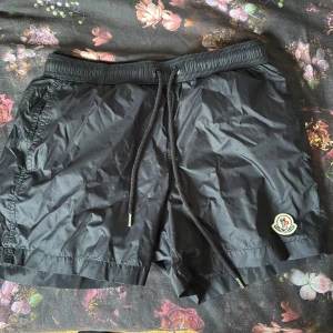 ÄKTA Svarta Moncler shorts funkar som badshorts - Nypris 2900kr. Svarta shorts från Moncler, passar alla från 165-175. Klassisk Moncler-logga på vänster ben. Lätta och snabbtorkande, perfekta för sommaren eller stranden. Snygg och enkel design som funkar till allt.  Går ner i pris vid snabb affär. NFC finns även