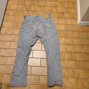 Grå relaxed jeans Jack & Jones 27/30 - Snygga grå jeans från Jack & Jones i modellen Relaxed/Chris. De har en avslappnad passform med raka ben och klassiska bakfickor. Tillverkade i mjukt bomullsjeansmaterial, perfekta för en chill och stilren look.