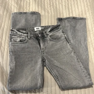 Grå bootcut jeans från 157 - Snygga grå jeans från 157 med bootcut-modell och låg midja. Jeansen har klassisk femficksdesign, tydliga sömmar och en cool tvättad look. Perfekta för dig som gillar en avslappnad men trendig stil.