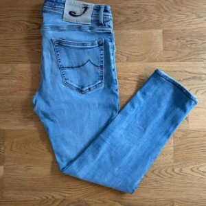 Herr Jacob Cohen Jeans - Snygga ljusblå jeansbyxor från Jacob Cohen, modell Style 622. Broderad J-logga på bakfickan och detaljerade knappar framtill. Längd 88 cm, bredd 42 cm. Storlek W33. Fraktar oftast samma dag!!