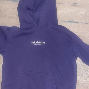 Lila hoodie från Originals Studio - Säljer en lila hoodie från Originals Studio med vit logga på bröstet. Klassisk modell med huva och magficka, perfekt för chill dagar. Mjuk och skön känsla, passar dig som gillar enkel och stilren streetwear.