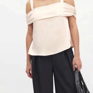 Champagnefärgad omlottopp med rosett - Snygg axelbandslös topp i champagnefärgad satin med breda axelband och omlottdetalj som knyts i en stor rosett bak. Toppen har en lyxig, glansig finish och en elegant offshoulder-look. Perfekt för dig som vill sticka ut med en chic och trendig vibe. 
