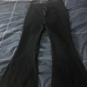Svarta bootcut jeans med rå kant - Säljer ett par svarta jeans med bootcut-modell och rå, fransig kant nertill. Jeansen har klassisk femficksdesign och stängs med dragkedja och knapp. Perfekta för dig som gillar en lite edgy och retro vibe.