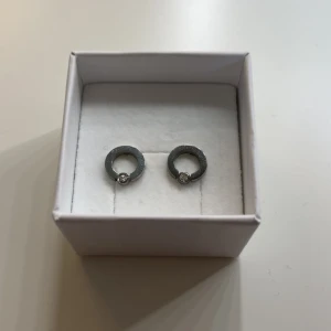 Runda silverörhängen med sten - Snygga örhängen i rund form av silverfärgat material med en liten glittrande sten i varje. Perfekta för dig som gillar stilrena och enkla smycken med en touch av bling.