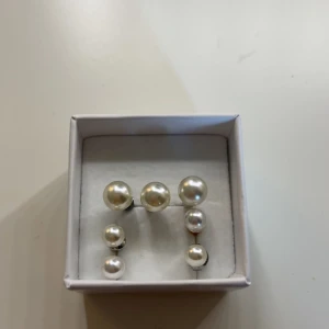 Dubbelpärlörhängen i silverfärg - Snygga örhängen med dubbla pärlor i olika storlekar. Klassisk vit pärlfinish och silverfärgad metall. Perfekt för dig som gillar stilrena accessoarer med en twist. Kommer i en liten ask.