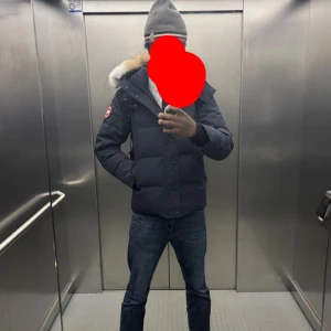 Canada Goose Wyndham Navy - Säljer en svart dunjacka från Canada Goose med huva och avtagbar pälskant. Jackan har dragkedja och knappar framtill samt klassisk logotyp på ärmen. Perfekt för kalla dagar och har en stilren, normal passform. Kvitto finns, använt i cirka 7-8 månader vintertid. I bra skick, inga anmärkelser