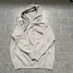 Ljusgrå hoodie med dragsko merinoull /bomull  - En stilren ljusgrå hoodie med huva och dragsko. Tröjan har långa ärmar och ribbade muddar vid ärmslut och nederkant. Perfekt för en avslappnad och bekväm stil.