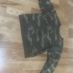 Grön camouflage sweatshirt från 157 - Säljer en grön sweatshirt med camouflage-mönster från 157. Tröjan har rund halsringning och långa ärmar. Perfekt för en avslappnad och cool stil.. använd ett få tal gånger.