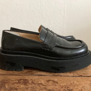 Svarta chunky loafers - Säljer ett par svarta loafers med chunky platt sula och klassisk design. Skorna har rund tå och är tillverkade skinn. Använda enstaka gånger. Har ett litet hälinlägg.