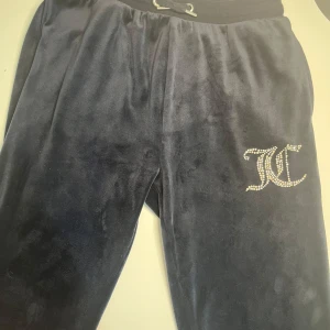 Juicy Couture mjukisbyxor med strasslogga - Mörkblå mjukisbyxor från Juicy Couture med glittrande strasslogga på ena benet. Byxorna har resår i midjan och är tillverkade i ett mjukt, sammetsliknande material som känns lyxigt och bekvämt. Säljer pga av att de inte passar mig. Priset kan diskuteras 💓🩷