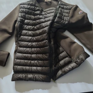 Brun pufferjacka från Moncler - Snygg brun pufferjacka från Moncler med quiltad framsida och släta ärmar. Jackan har dragkedja och Moncler-logga på ena ärmen. Perfekt för kyliga dagar och har en modern, sportig look.