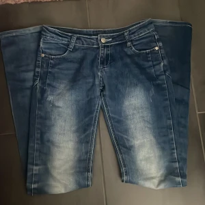 Blå lågmidjade jeans från Piano - Säljer ett par blå jeans från Piano. Byxorna har en lätt tvättad look och lätt utsvänga ben. 