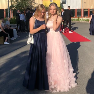 Ljusrosa balklänning med blomdetaljer - Säljer en romantisk ljusrosa balklänning med tunna axelband och blomdetaljer nertill. Klänningen har en elegant, utsvängd kjol och är perfekt för bal eller fest. Materialet är lätt och ger en drömmig känsla. Endast använd en gång så väldigt bra skick! Finns i Luleå 