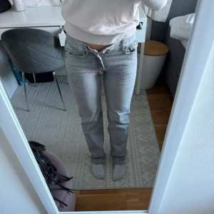 Ljusgrå raka jeans - Säljer ett par ljusgrå jeans med rak passform och klassisk femficksdesign. Byxorna har normal midja och stängs med dragkedja och knapp. Perfekta till vardags för en avslappnad stil.