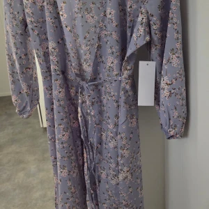 Blå blommig omlottklänning - Superfin blå omlottklänning med små blommor i rosa och vitt. Klänningen har långa ärmar, knytband i midjan och en luftig känsla. Perfekt för vår och sommar! 🌸 Ny med lapp kvar.