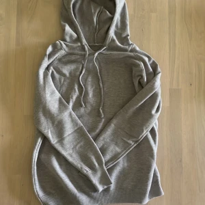 Merinoull hoddie grå - Säljer en stilren ljusgrå stickad hoodie med huva och dragsko. Tröjan har långa ärmar och ribbade muddar vid ärmslut och nederkant. Perfekt för en avslappnad och snygg look. Storlek M men sitter som en S