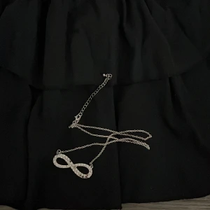 Silverfärgat halsband med oändlighetstecken - Säljer ett stilrent halsband i silverfärg med ett oändlighetstecken dekorerat med små glittrande stenar. Kedjan är tunn och smidig, perfekt för att ge en extra touch till din outfit.
