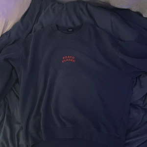 Mörkblå sweatshirt med tryck 'Peace Please' - Mörkblå sweatshirt från junkyard med rött tryck 'Peace Please' på bröstet och stort tryck av jordglob och text på ryggen. Klassisk rund hals och långa ärmar. Perfekt för en avslappnad stil.