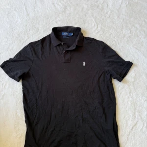Polo Ralph Lauren Piké Svart M - Säljer en svart Ralph Lauren piké med röd logga i storlek M, finns ett litet hål i nacken plus några fläckar men går säkert bort efter en tvätt eller två ! 😊