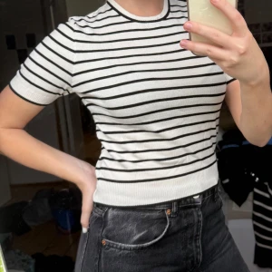 Vit och svart randig stickad tröja från H&M - Säljer en vit stickad tröja med svarta horisontella ränder från H&M. Tröjan har korta ärmar, rund halsringning och ribbade muddar vid ärmslut och nederkant. Perfekt för en stilren och enkel look. Helt oanvänd med lappen kvar