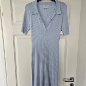 Ljusblå klänning från Neo Noir - Säljer en ljusblå ribbad klänning från Neo Noir med krage och v-ringning. Klänningen har korta ärmar och är tillverkad i ett stretchigt material som ger en snygg passform. Perfekt för vår och sommar!