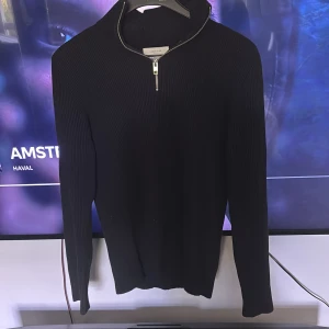 Svart stickad tröja med dragkedja från Jack & Jones - Säljer en svart stickad tröja från Jack & Jones med halv dragkedja vid halsen. Tröjan har lång ärm och en ribbad struktur som ger en snygg och stilren look. Perfekt för lager-på-lager under kyligare dagar.