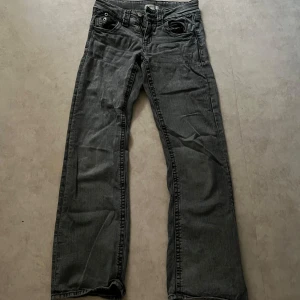 Grå jeansbyxor från Gina Tricot - Säljer ett par grå jeansbyxor från Gina Tricot i klassisk modell. Byxorna har normal passform, raka ben och detaljer med knappar och dragkedja framtill. Perfekta för en avslappnad stil.