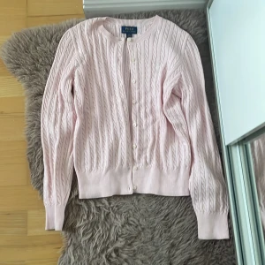 Ljusrosa kabelstickad kofta från Polo Ralph Lauren - Säljer en super fin ljusrosa kabelstickad kofta från Polo Ralph Lauren. Koftan har rund hals, långa ärmar och är i storlek 12-14år. Mycket bra skick och är aldrig använd. Hör av dig om du har frågor eller funderingar💕