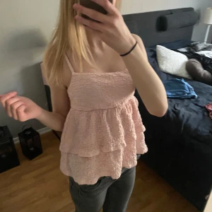 Ljusrosa volangig linnetopp - Söt ljusrosa linnetopp med volanger och smala axelband. Toppen har en lös passform och är tillverkad i ett lätt, strukturerat tyg som ger en romantisk känsla.