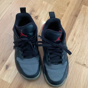 Svarta och gråa sneakers från Jordan Mars - Säljer ett par Jordan Mars sneakers i svart och grått med röda detaljer och genomskinlig sula. Skorna har snörning, rund tå och är tillverkade i syntetmaterial och textil. Perfekta för dig som gillar streetwear och sportig stil.