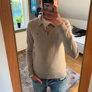 Beige pikétröja från Morris - Säljer en stilren beige pikétröja från Morris med klassisk krage och knappar framtill. Tröjan har långa ärmar och diskret broderad logga på bröstet. Perfekt för en clean och avslappnad look. Nypris är 1599