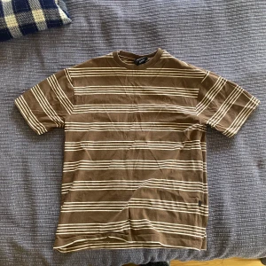 Brun och vit randig t-shirt från Sweet SKTBS - Säljer en brun t-shirt med vita horisontella ränder från Sweet SKTBS. T-shirten har normal passform och är kortärmad. Tillverkad i mjuk bomull för extra komfort. Använd fåtal gånger.