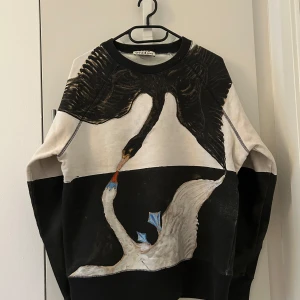 Acne studios Svart och vit sweatshirt med svanmotiv - Unik sweatshirt från Acne Studios med stort tryck av två svanar på framsidan. Tröjan är svart och vit med rund halsringning och långa ärmar. Perfekt statement-plagg för dig som gillar konstnärliga prints.