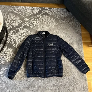 Mörkblå pufferjacka från Emporio Armani EA7 - Säljer en mörkblå pufferjacka från Emporio Armani EA7.jackan är praktiskt använt seriöst i nytt skick,säljer föratt jag använder inte den och tyckte jag spenderade onödigt mycket på den men aja.Den är helt äkta och är storlek S men kan passa M. Hör av er för flera frågor!!
