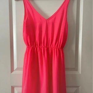 Rosa ärmlös klänning med v-ringning - Säljer en snygg rosa klänning med v-ringad hals och resår i midjan. Klänningen är ärmlös och har en luftig passform, perfekt för varma dagar. Enkel och stilren design som passar till många tillfällen.