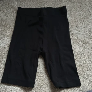 Svarta cykelshorts från Kappahl - Svarta cykelshorts från Kappahl med midja i resår och knälång passform. Perfekta för träning eller som ett basplagg till sommaren. Gjorda i mjukt och stretchigt material för extra komfort.