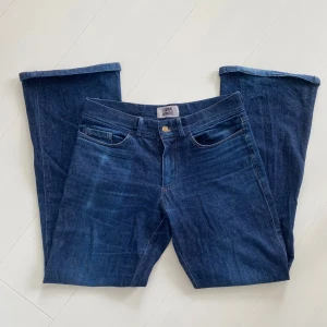 Mörkblå indigo bootcut jeans från Carnal Apparel - Snygga mörkblå jeans från Carnal Apparel med klassisk femficksdesign och bootcut-ben. Jeansen har normal passform och är tillverkade i ett mjukt denimtyg. Perfekta för dig som gillar en tidlös stil med lite utsvängda ben. Nypris 2500kr.