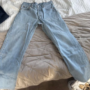 Ljusblå Levis 501 jeans - Klassiska ljusblå Levis 501 jeans med raka ben och femficksmodell. Byxorna har knappgylf och den ikoniska Levis-lappen bak i midjan. Perfekta för en avslappnad och tidlös stil.