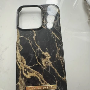 Svart och guld marmormönstrat mobilskal från iDeal of Sweden - Snyggt mobilskal från iDeal of Sweden med svart och guld marmormönster. Skalets design ger en lyxig känsla och har en metallbricka med varumärkets logga längst ner. Perfekt för dig som vill ha en trendig accessoar till mobilen.